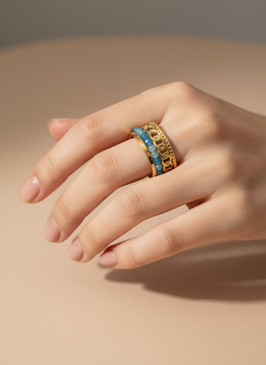 Bague Julia dorée à trois anneaux avec chaîne, perles bleues et anneau texturé sur fond blanc