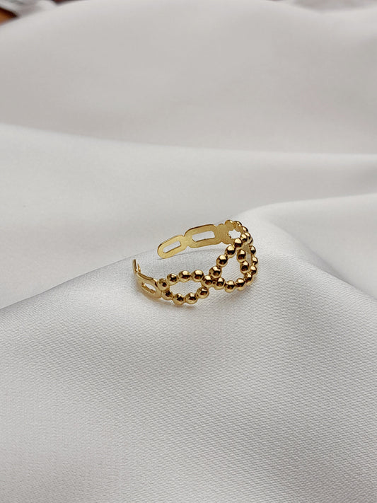 Bague dorée ajourée formée de petites perles dorées, posée sur un tissu blanc élégant.