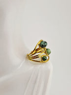 Bague dorée en acier inoxydable avec trois pierres vertes rondes sur présentoir blanc