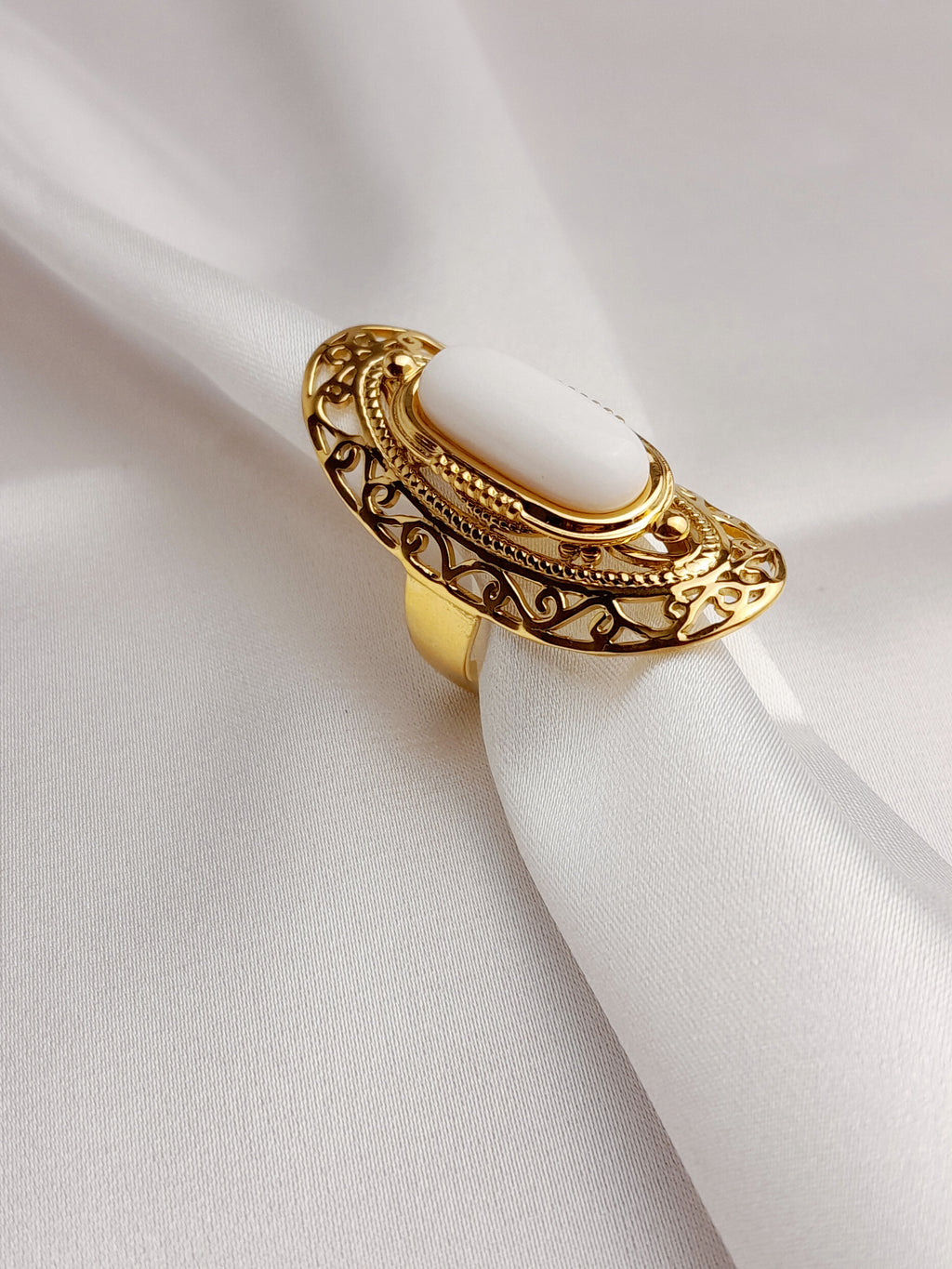 Bague Selena dorée en acier inoxydable avec pierre blanche ovale sur fond satiné