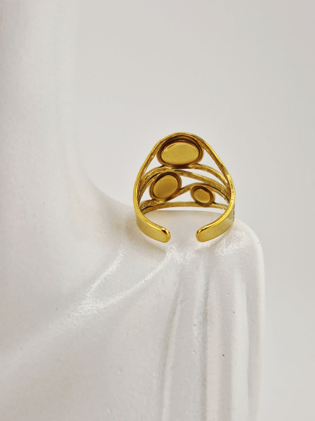 Bague dorée en acier inoxydable avec trois pierres vertes rondes sur présentoir blanc