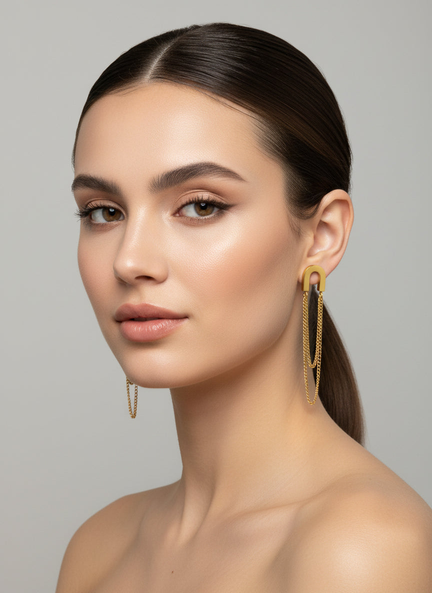 Boucles d’oreilles dorées minimalistes à chaînes pendantes porté en acier inoxydable, présentées sur un présentoir blanc design.