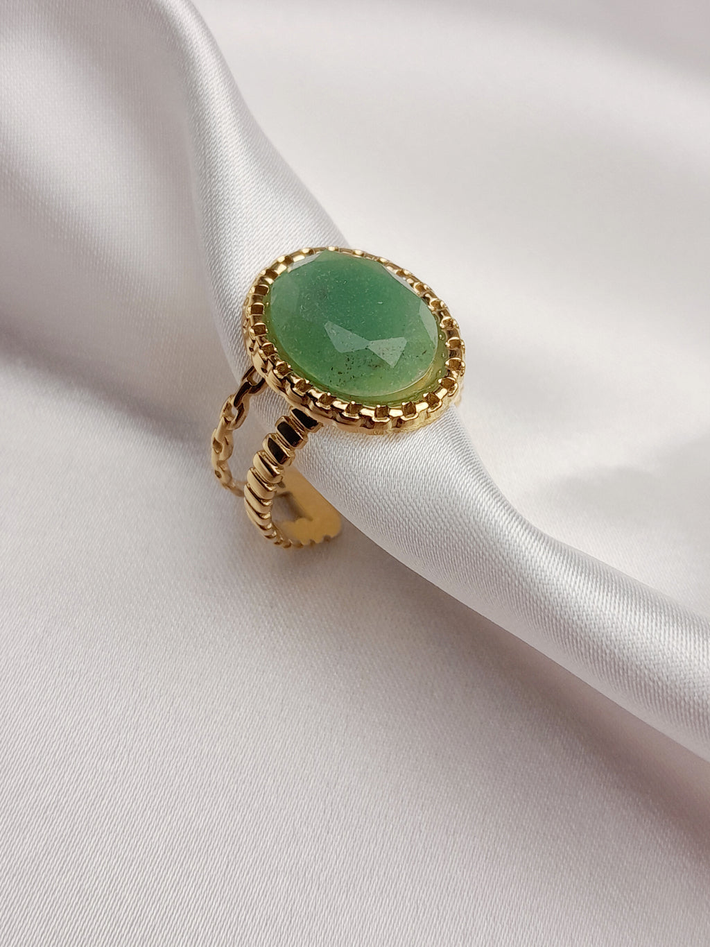 Bague Céleste dorée en acier inoxydable avec pierre verte ovale sur tissu blanc.