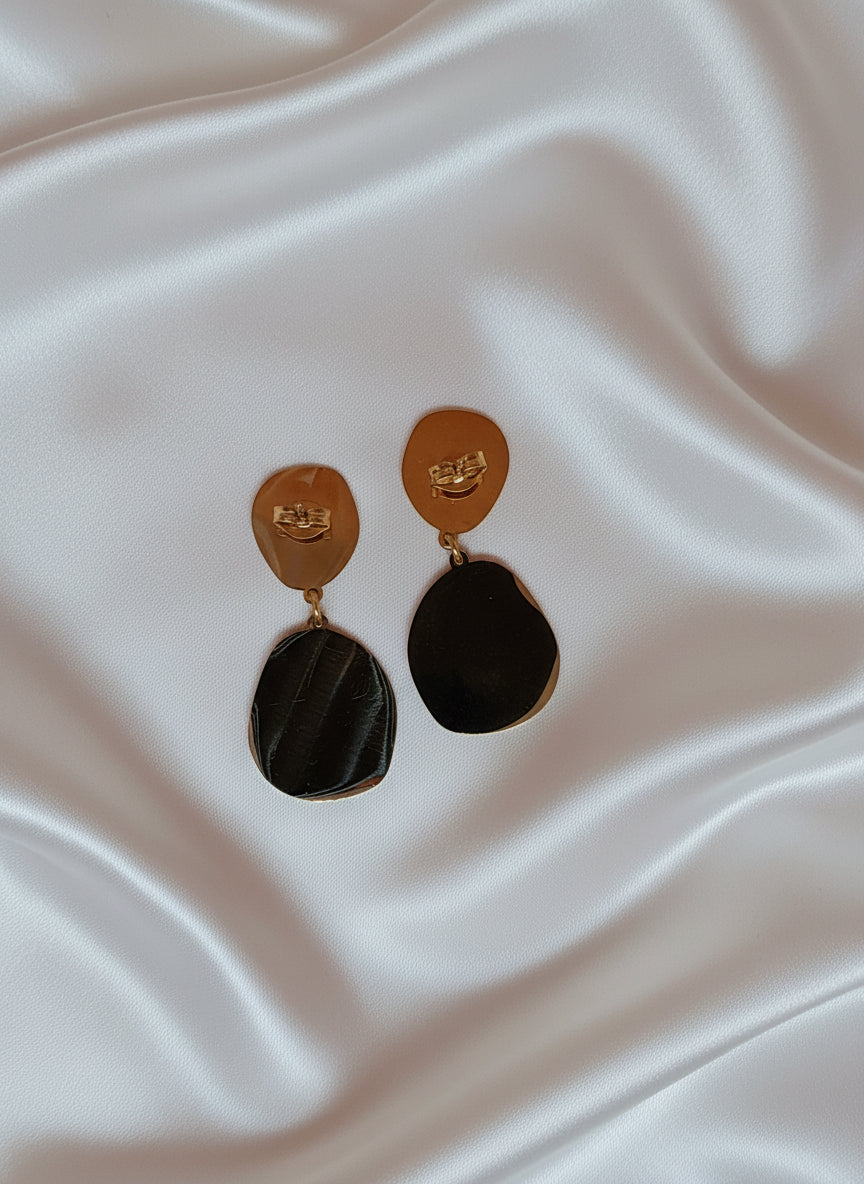 Boucles d’oreilles Soline dorées à double pampille ovale texturée posées sur tissu satiné blanc.