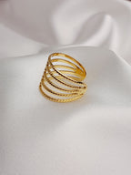 Bague dorée à plusieurs rangs texturés et entrelacés, posée sur un tissu blanc satiné.