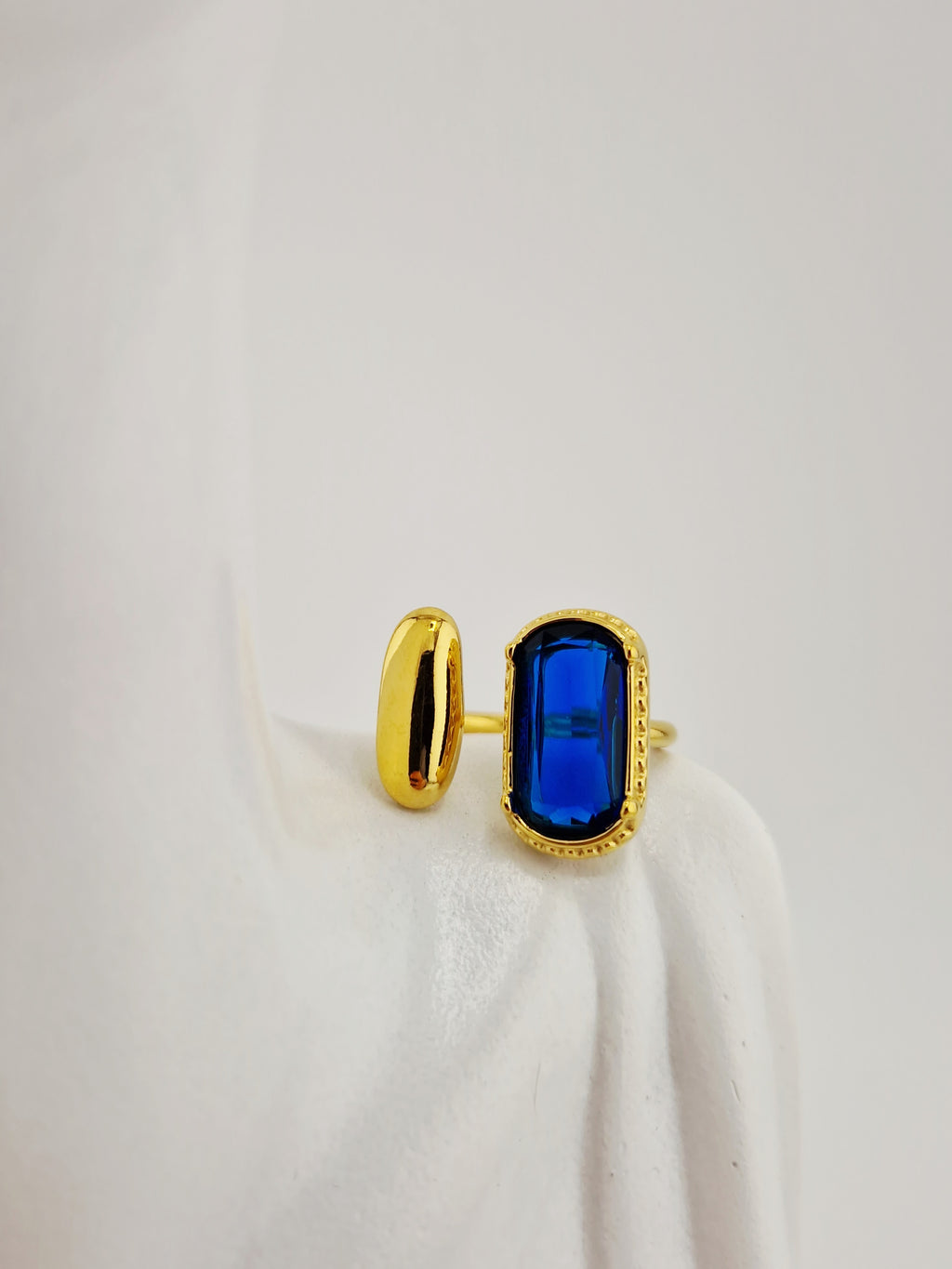 Bague dorée Gina en acier inoxydable avec pierre rectangulaire bleue sur fond neutre