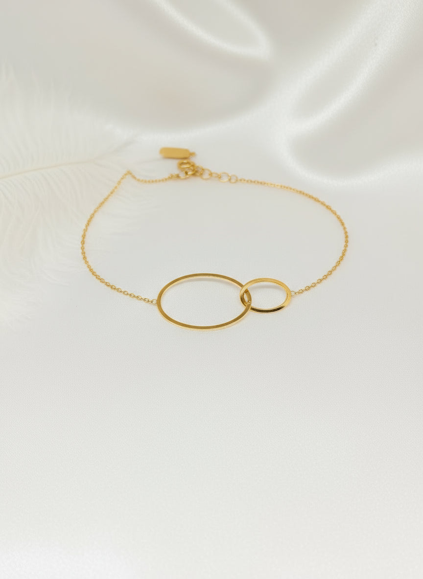 Bracelet Lénae doré à deux anneaux entrelacés en acier inoxydable, taille 16+ cm, posé sur un tissu blanc satiné. 
