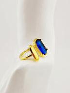 Bague dorée Gina en acier inoxydable avec pierre rectangulaire bleue sur fond neutre