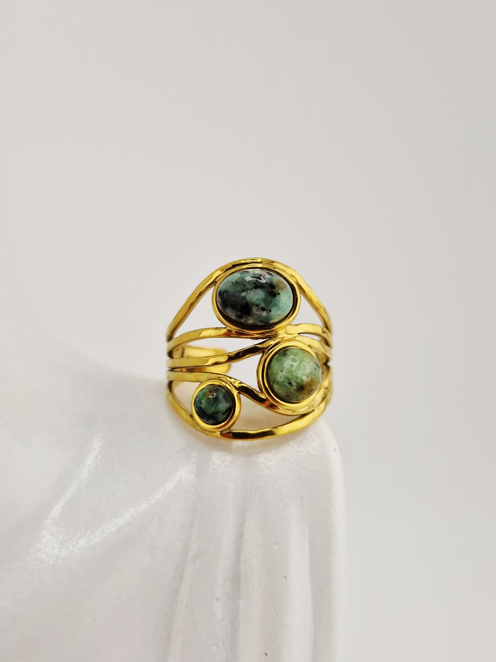 Bague dorée en acier inoxydable avec trois pierres vertes rondes sur présentoir blanc
