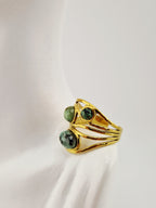 Bague dorée en acier inoxydable avec trois pierres vertes rondes sur présentoir blanc