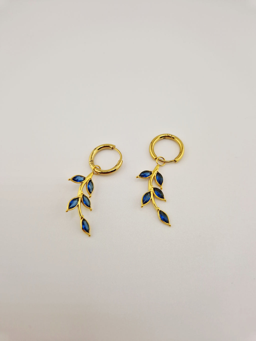 Boucles d’oreilles Éléa en acier inoxydable doré avec pendentif branche et pierres bleues.