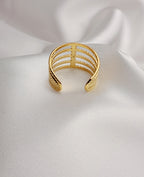 Bague dorée à plusieurs rangs texturés et entrelacés, posée sur un tissu blanc satiné.