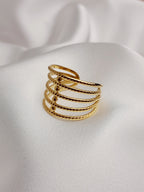 Bague dorée à plusieurs rangs texturés et entrelacés, posée sur un tissu blanc satiné.