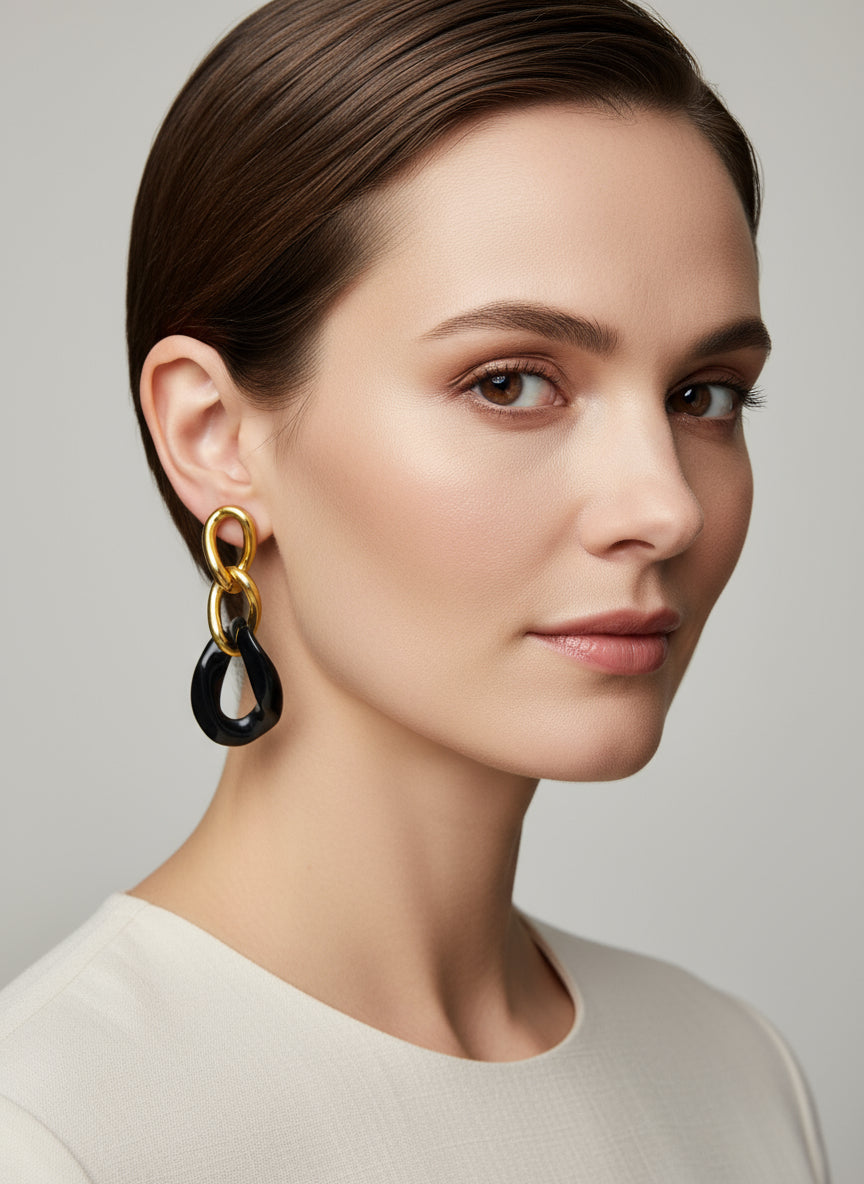 Boucles d’oreilles Yumi en acier inoxydable doré avec pendentifs noirs porté sur fond clair