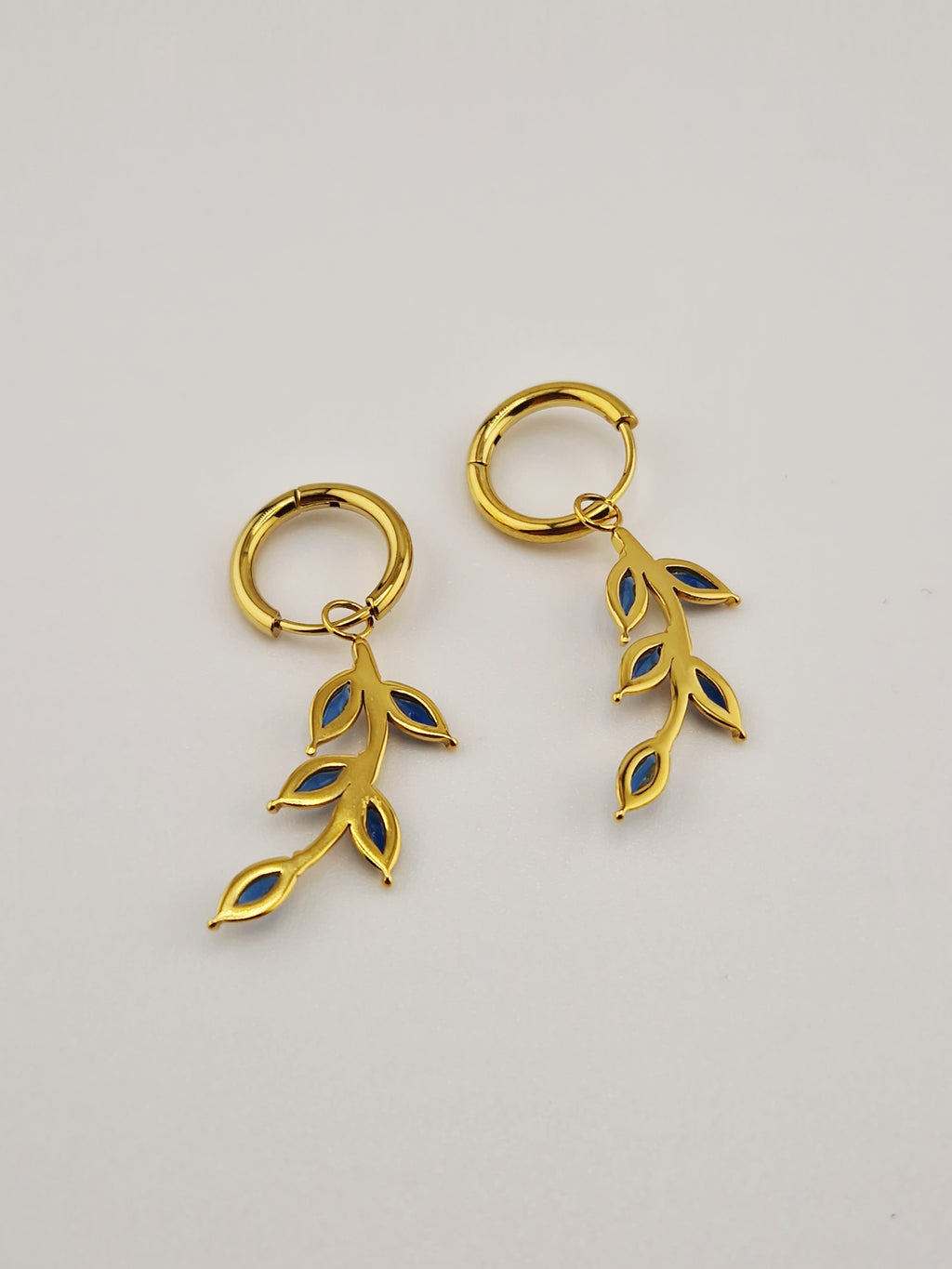 Boucles d’oreilles Éléa en acier inoxydable doré avec pendentif branche et pierres bleues.