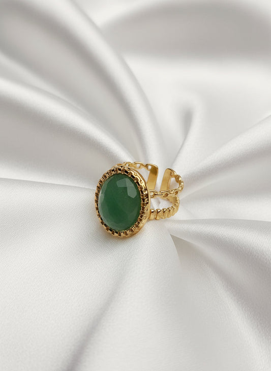 Bague Céleste dorée en acier inoxydable avec pierre verte ovale sur tissu blanc.