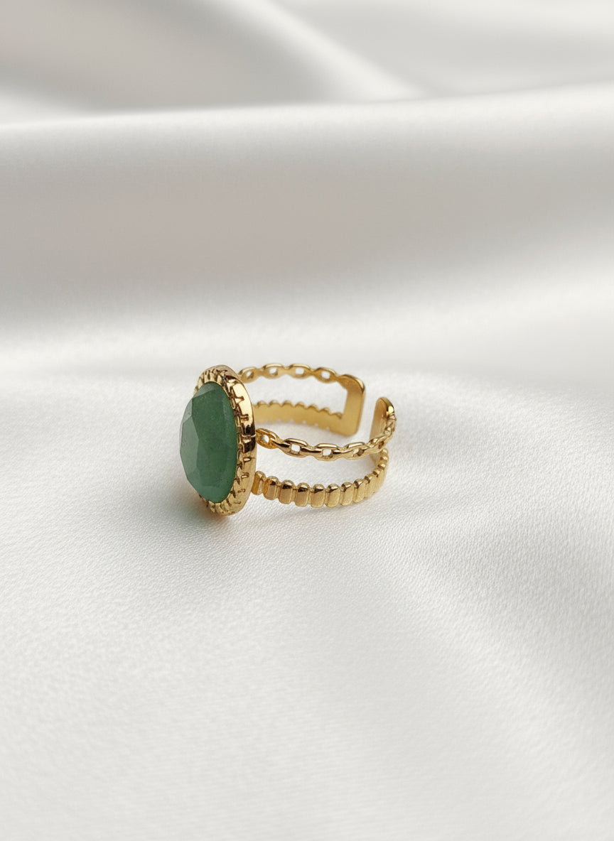 Bague Céleste dorée en acier inoxydable avec pierre verte ovale sur tissu blanc.