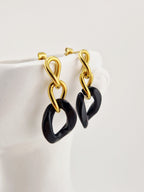 Boucles d’oreilles Yumi en acier inoxydable doré avec pendentifs noirs  sur fond clair