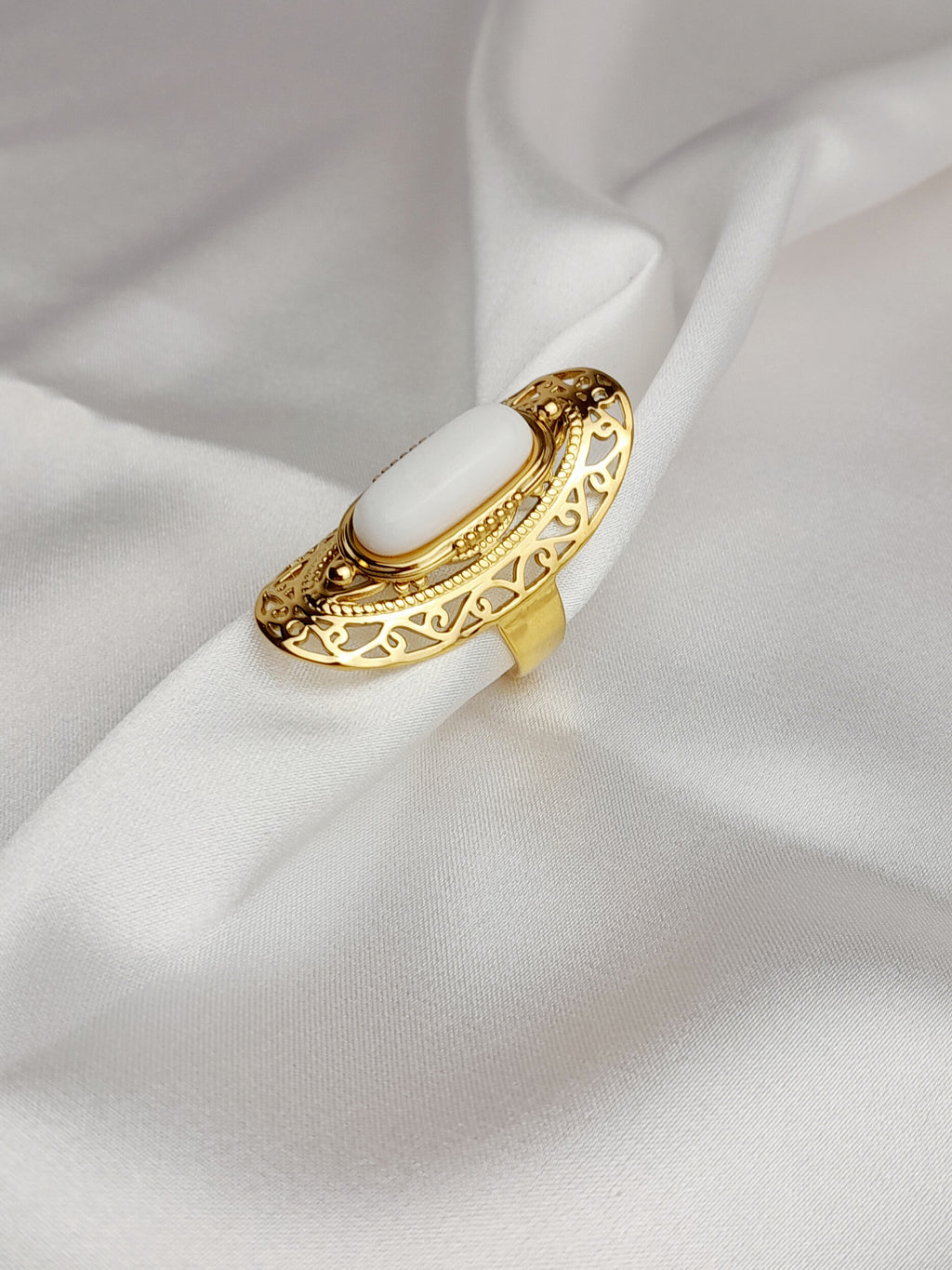 Bague Selena dorée en acier inoxydable avec pierre blanche ovale sur fond satiné