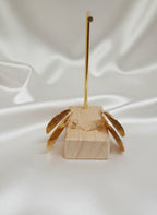 Boucles d’oreilles Daphné dorées en acier inoxydable à texture martelée et surface polie, posées sur fond rose satiné avec plume blanche. 