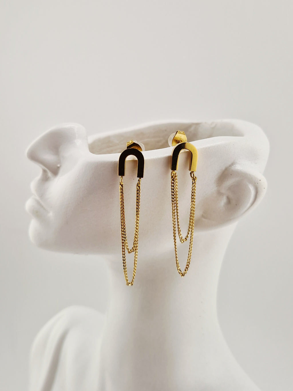 Boucles d’oreilles dorées minimalistes à chaînes pendantes en acier inoxydable, présentées sur un présentoir blanc design.