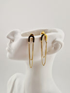 Boucles d’oreilles dorées minimalistes à chaînes pendantes en acier inoxydable, présentées sur un présentoir blanc design.